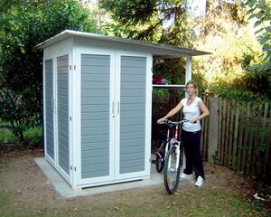 Eine Person steht mit einem Fahrrad vor einem kleinen Schuppen im Garten.
