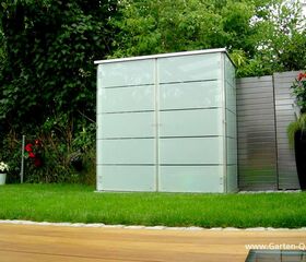 . Ein moderner Gartenschrank mit Glasfronten steht auf Rasen, umgeben von Pflanzen und Holzboden.