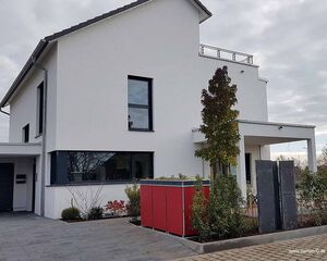 Ein modernes weißes Haus mit großen Fenstern, einem roten Schuppen und einem kleinen Garten davor.