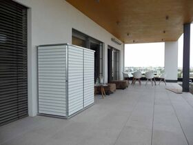 . Ein Balkon mit modernen weißen Möbeln, Tisch und Stühlen, sowie einem verschlossenen Schrank an der Wand.