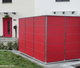 . Ein roter Gartenschrank steht vor einer weißen Hauswand mit roter Tür und einem Briefkasten.