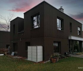 . Ein modernes Haus mit Holzfassade und großem Garten, Abendhimmel im Hintergrund.