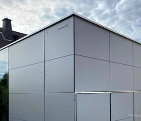 Ein modernes Gartenhaus mit grauen Paneelen neben einem Haus.