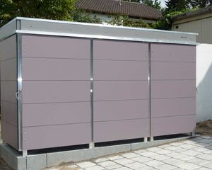 . Ein großer, grauer Außenschrank steht auf gepflastertem Boden neben einer weißen Mauer.